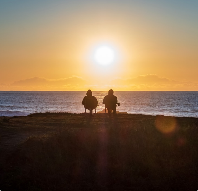 Two people watch the sunrise or sunset over a body of water