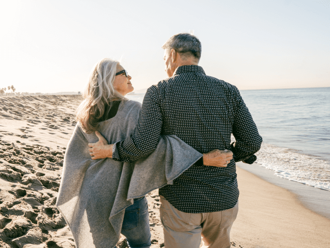 A couple with gray hair walk along the beach